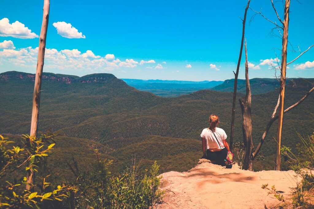 woman sitting on ground watching mountain during daytime, Natural Wonders Of Australia