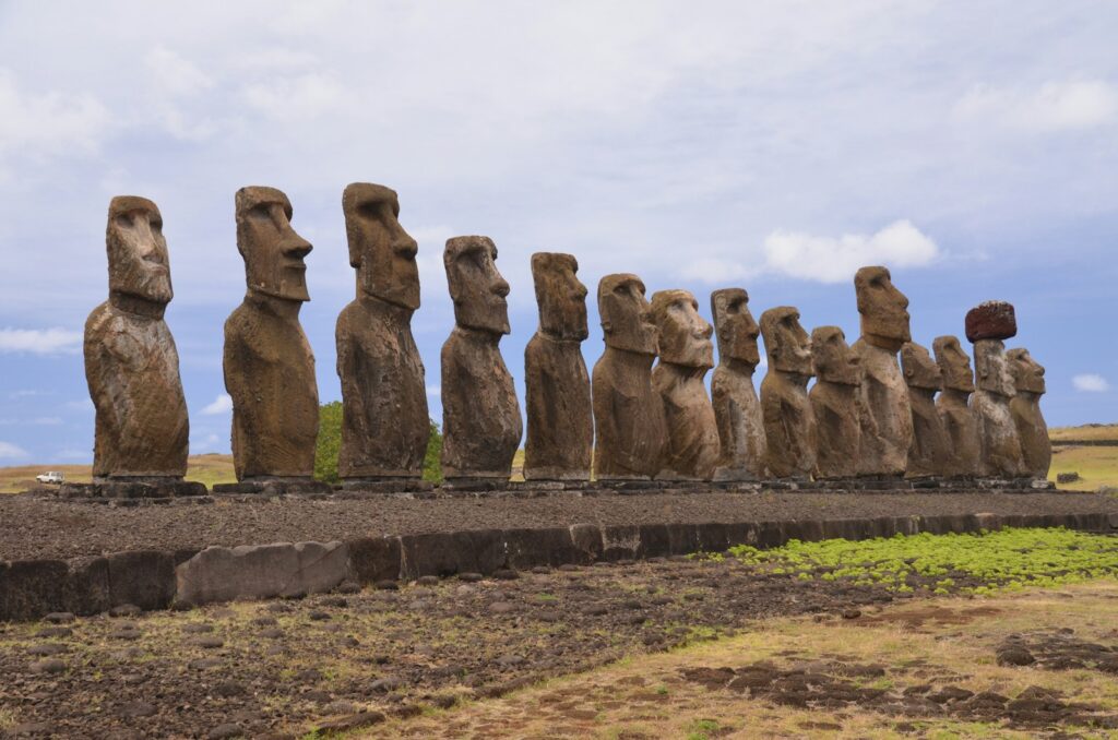 a row of moai statues sitting on top of a grass covered field, Top Ten Wonders of the World 